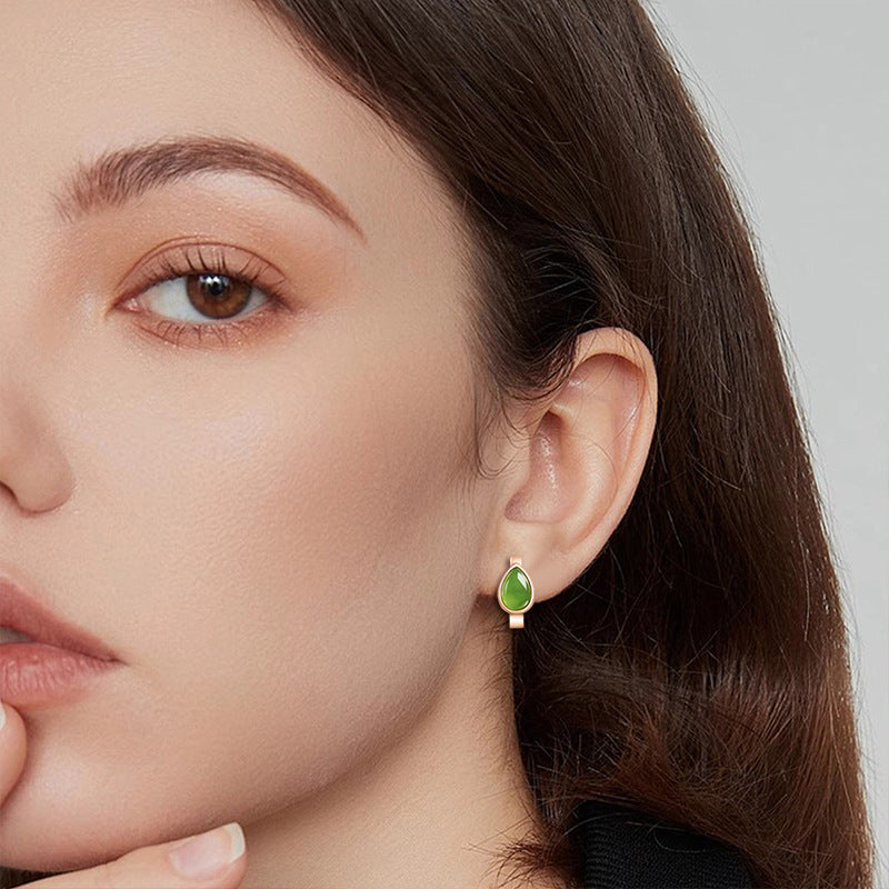Close-up of a woman wearing a green earring with a neutral background